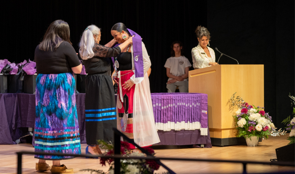 Kathy places a stole on a student's shoulders on stage