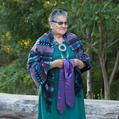 Bertha Skye standing outdoors smiling and holding a purple silk convocation stole 