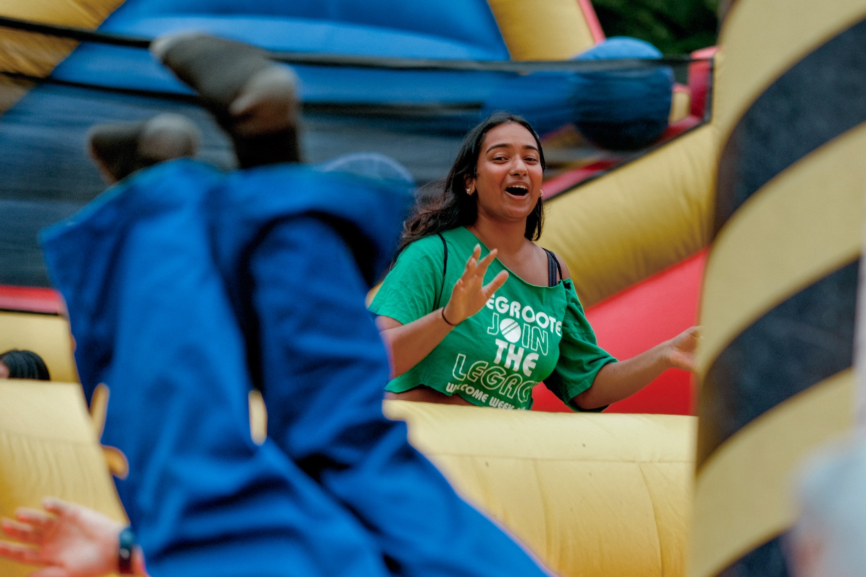 A person on a bouncy castle laughs in the background. in the foreground, you can see the legs and feet of someone who has fallen over on the castle.