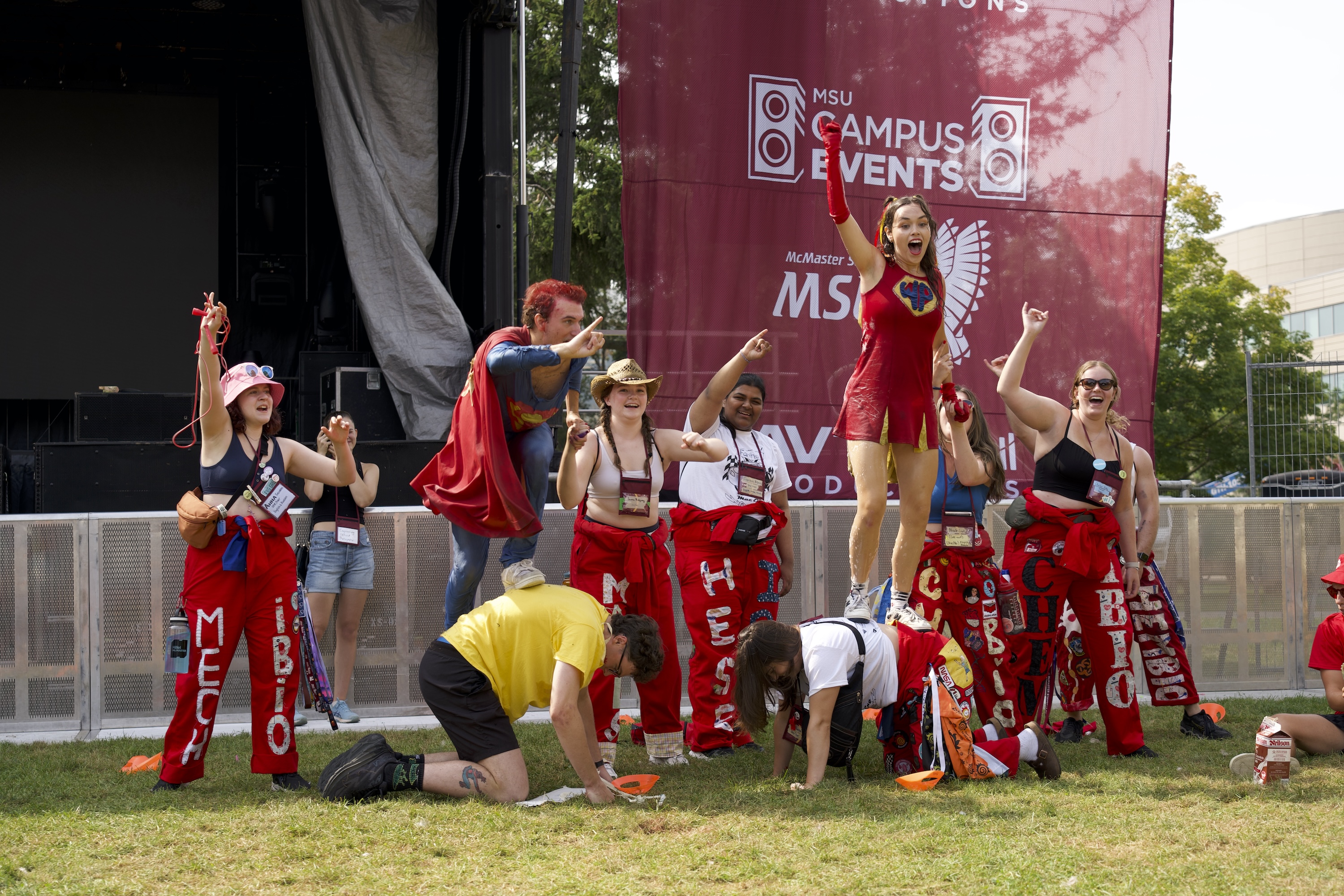 A group of Engineering reps, some dressed as superheroes, stand on each other's backs and cheer.