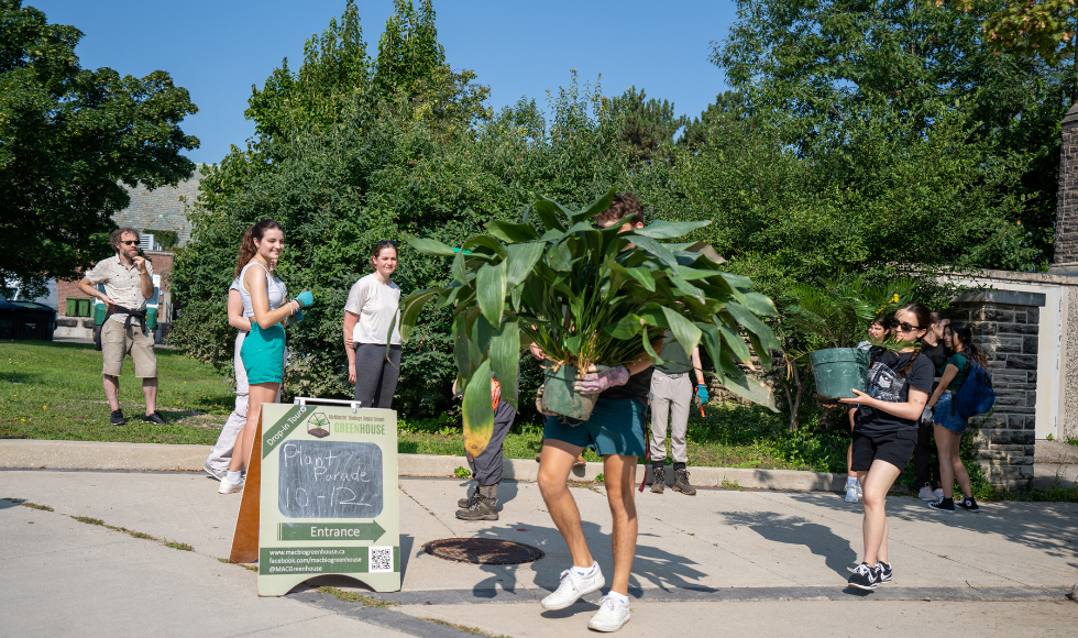 Two people carrying potted plants while others look on