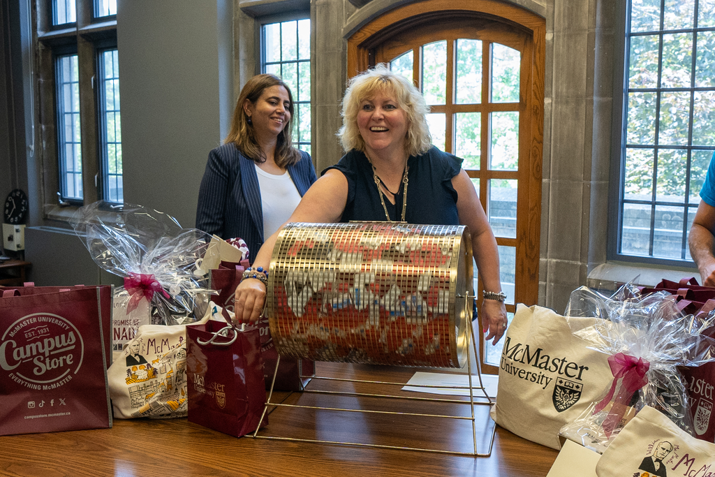 Susan Tighe and Saher Fazilat smile as Tighe rolls the drum holding raffle tickets