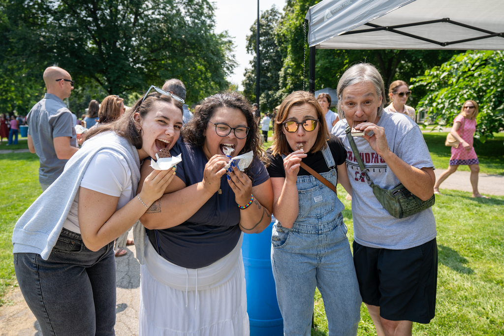 Four staff members pose for a picture while taking big chomps out of their popsicles at the ice cream social