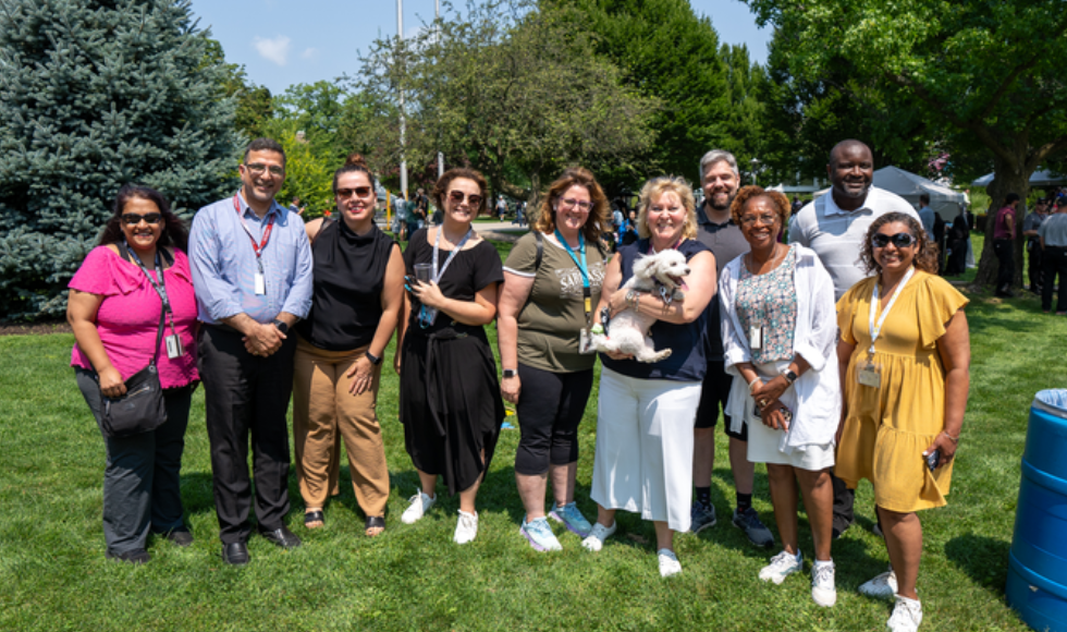 A smiling group of McMaster faculty and staff with Provost Susan Tighe, who is holding a dog.