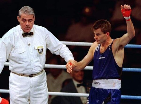 A boxing referee raises the arm of a boxer in a victory pose inside a boxing ring. 