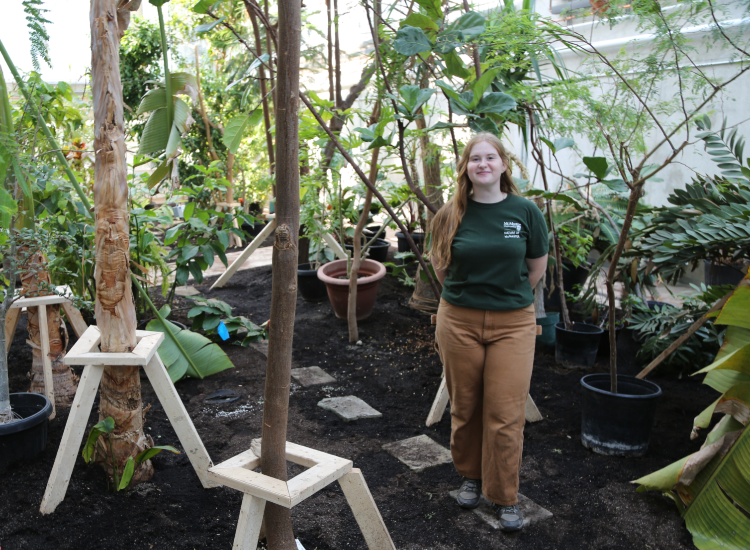 Full length photo of Renee Twyford in the new greenhouse, surrounded by trees and plants that were recently moved here.