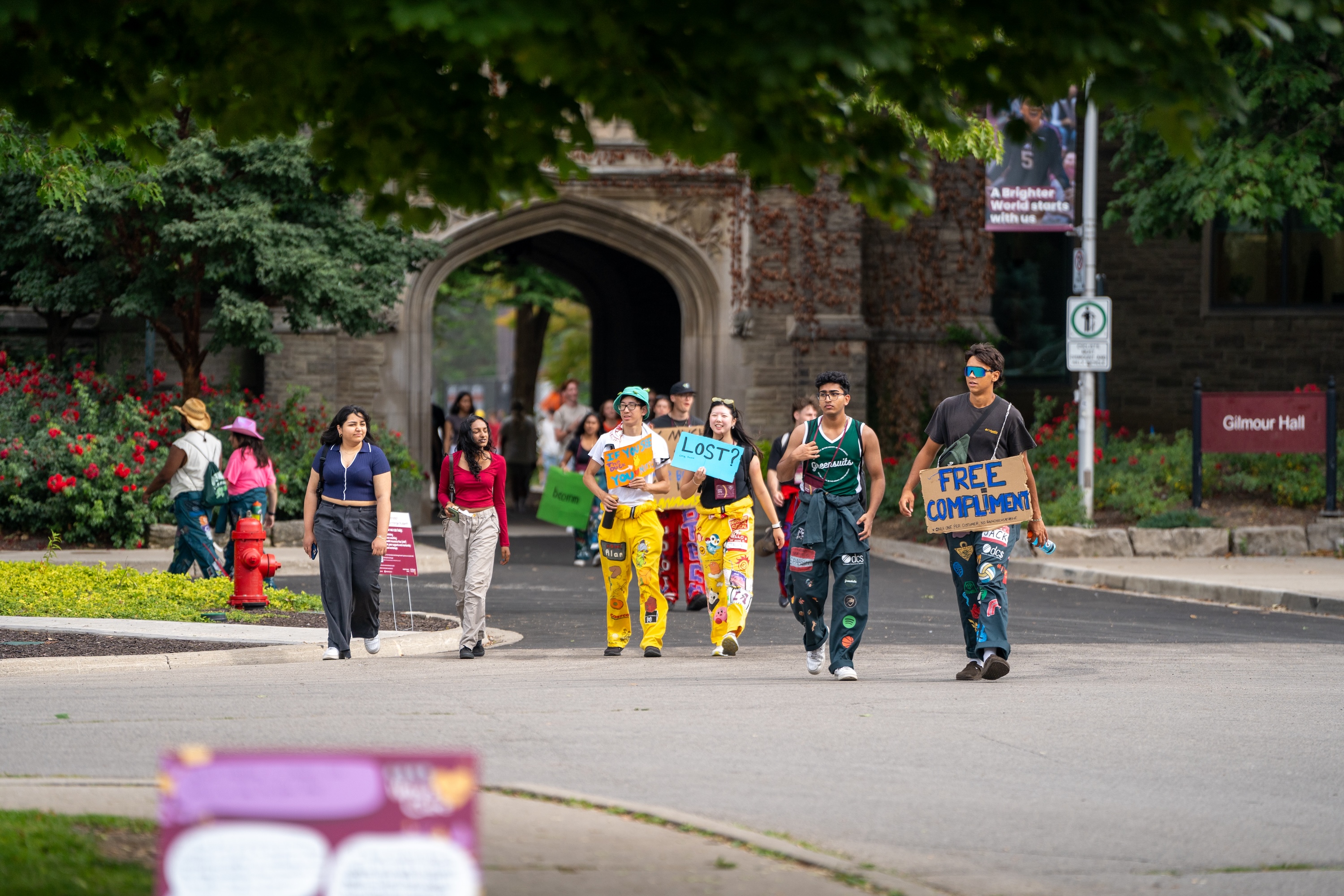 A group of WW reps in different coloured jumpsuits walk across campus holding signs and smiling.