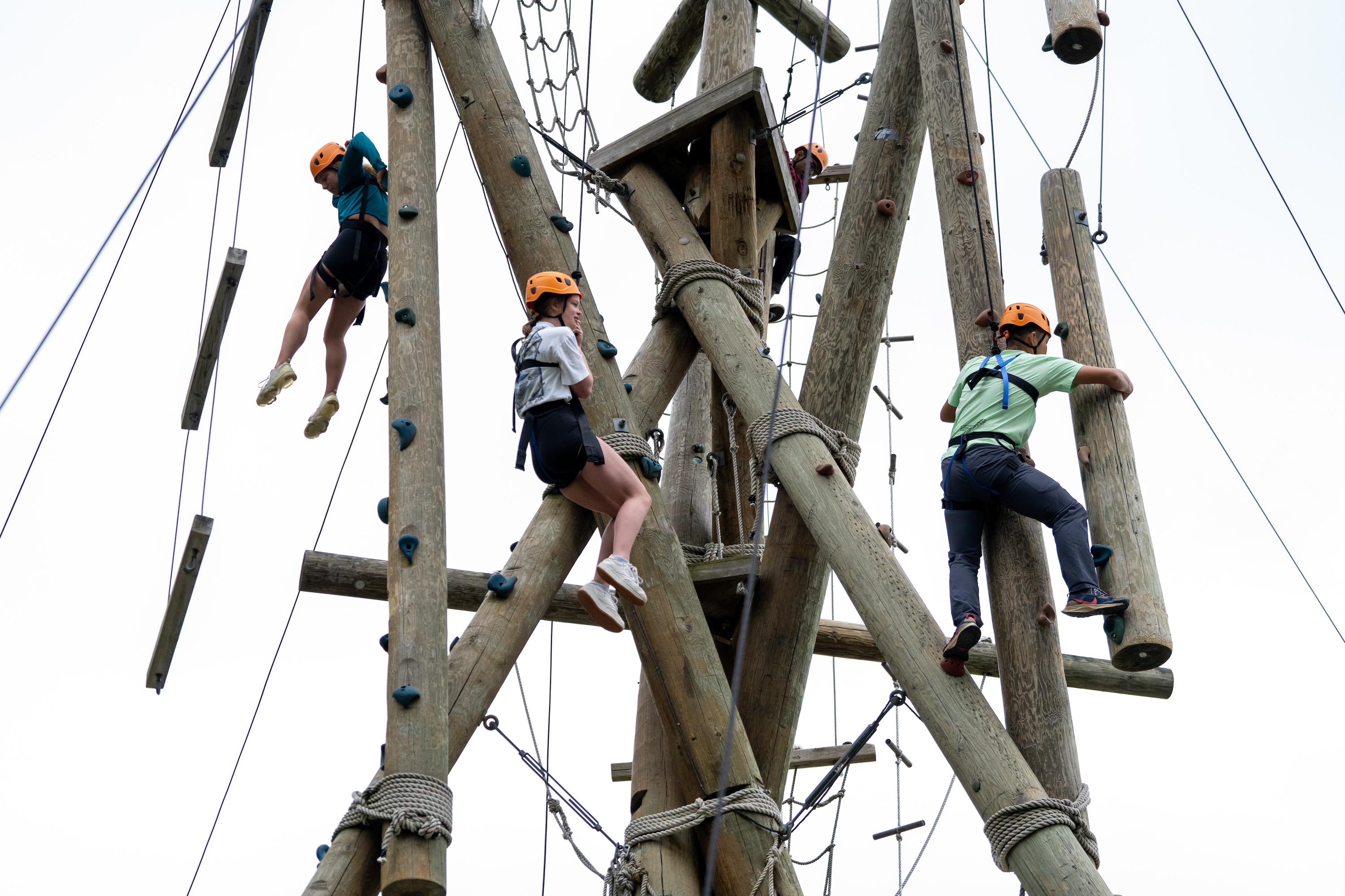 Seen from below: Three people in helmets and climbing harnesses at the top of the altitude climbing tower.