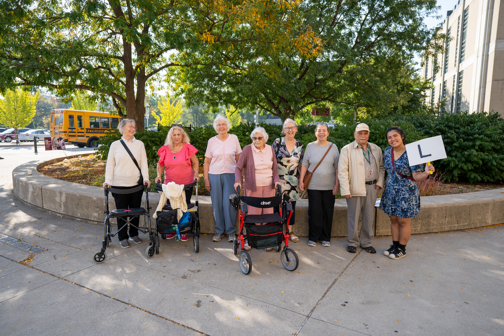 A group of seven older adults and a student stand in a row smiling at the camera. 