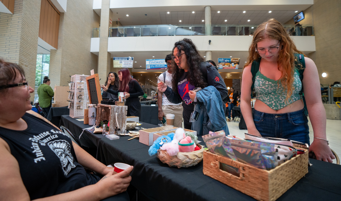 People stop to look at Indigenous-made crafts for sale at a table in the atrium of MUSC