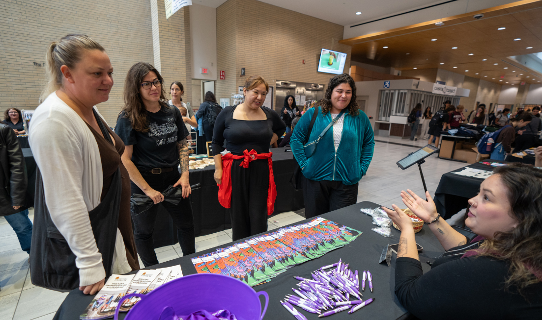 A group of smiling people stand around a table at the vendor market in MUSC