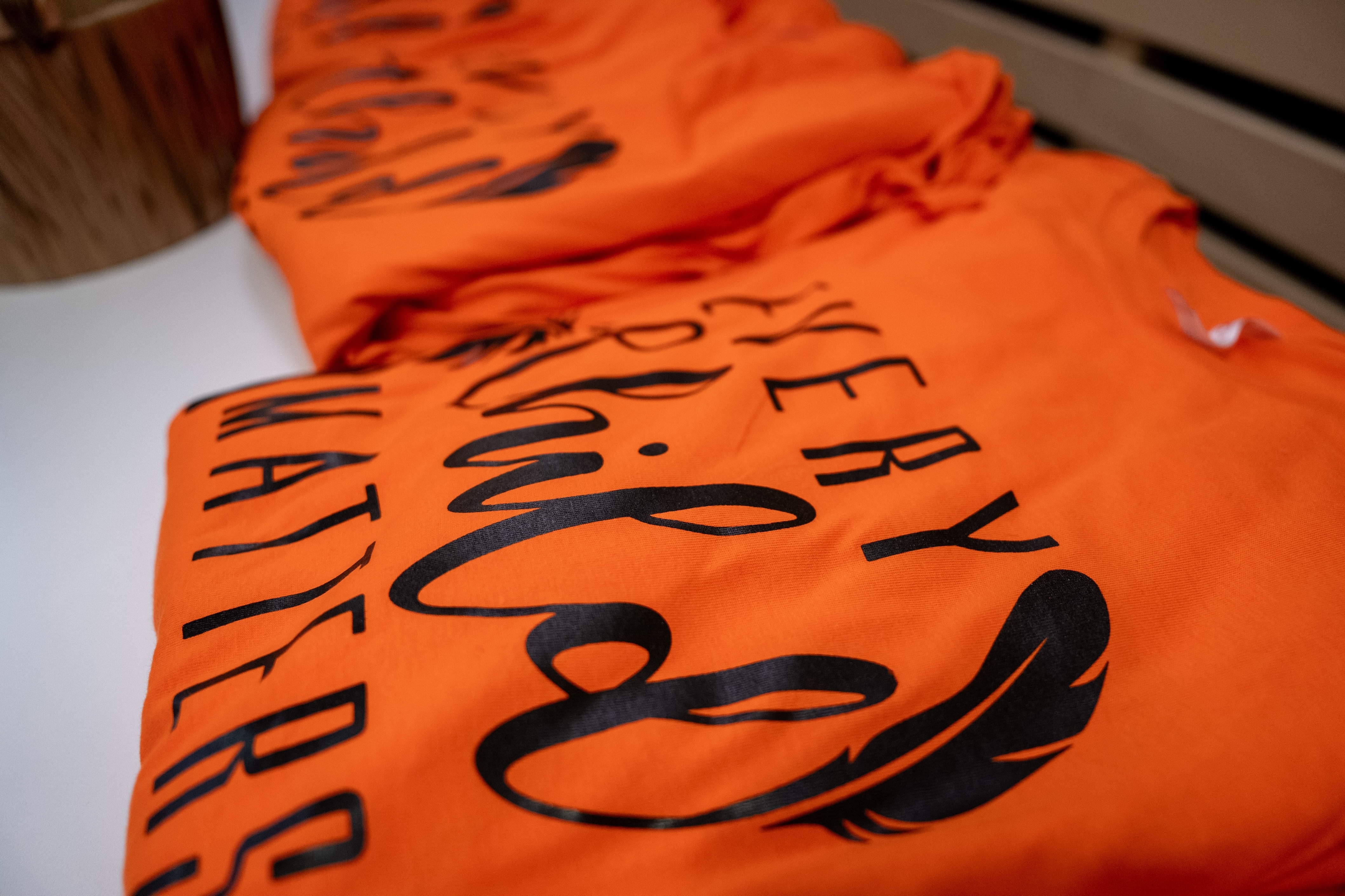 Folded Orange T shirts on a table, with black writing on them that reads "Ever Child Matters"