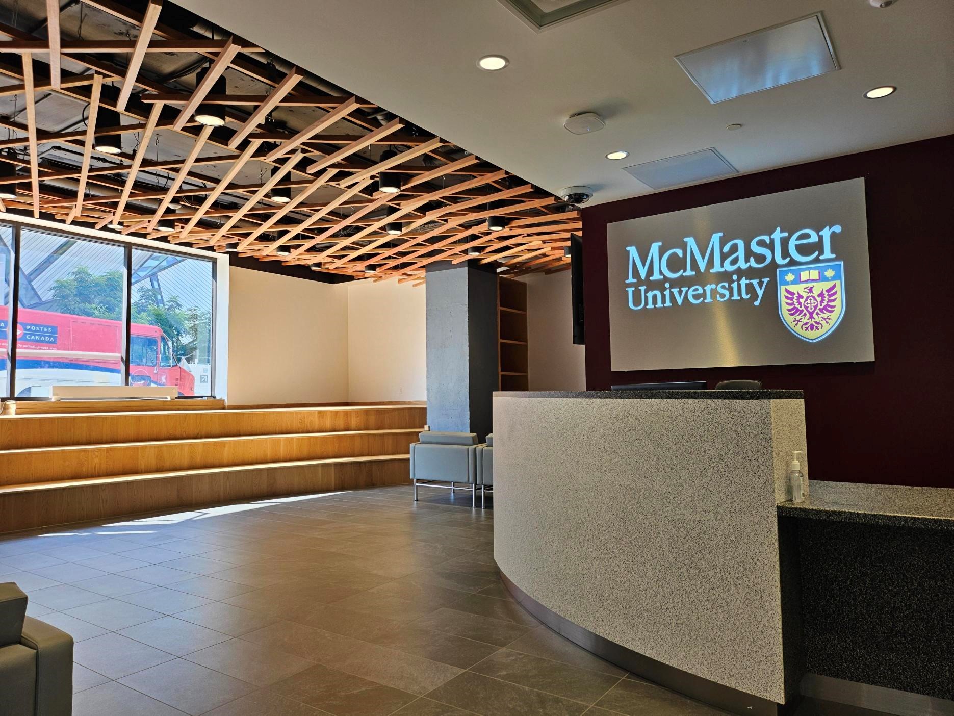 A lobby with a screen displaying the McMaster University logo. There is a large window and the Royal Ontario Museum can be seen in the distance. 