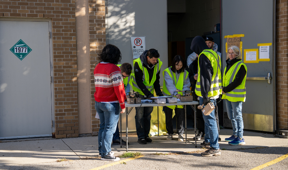 A handful of people, most in fluorescent yellow safety vests, working over a table that has some technical equipment on it.