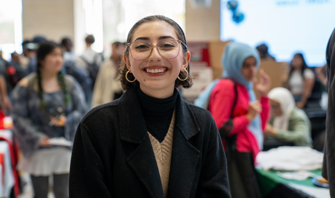 A student with dark hair and a dark coat smiles widely while standing at 2024 Cultural Fest in MUSC