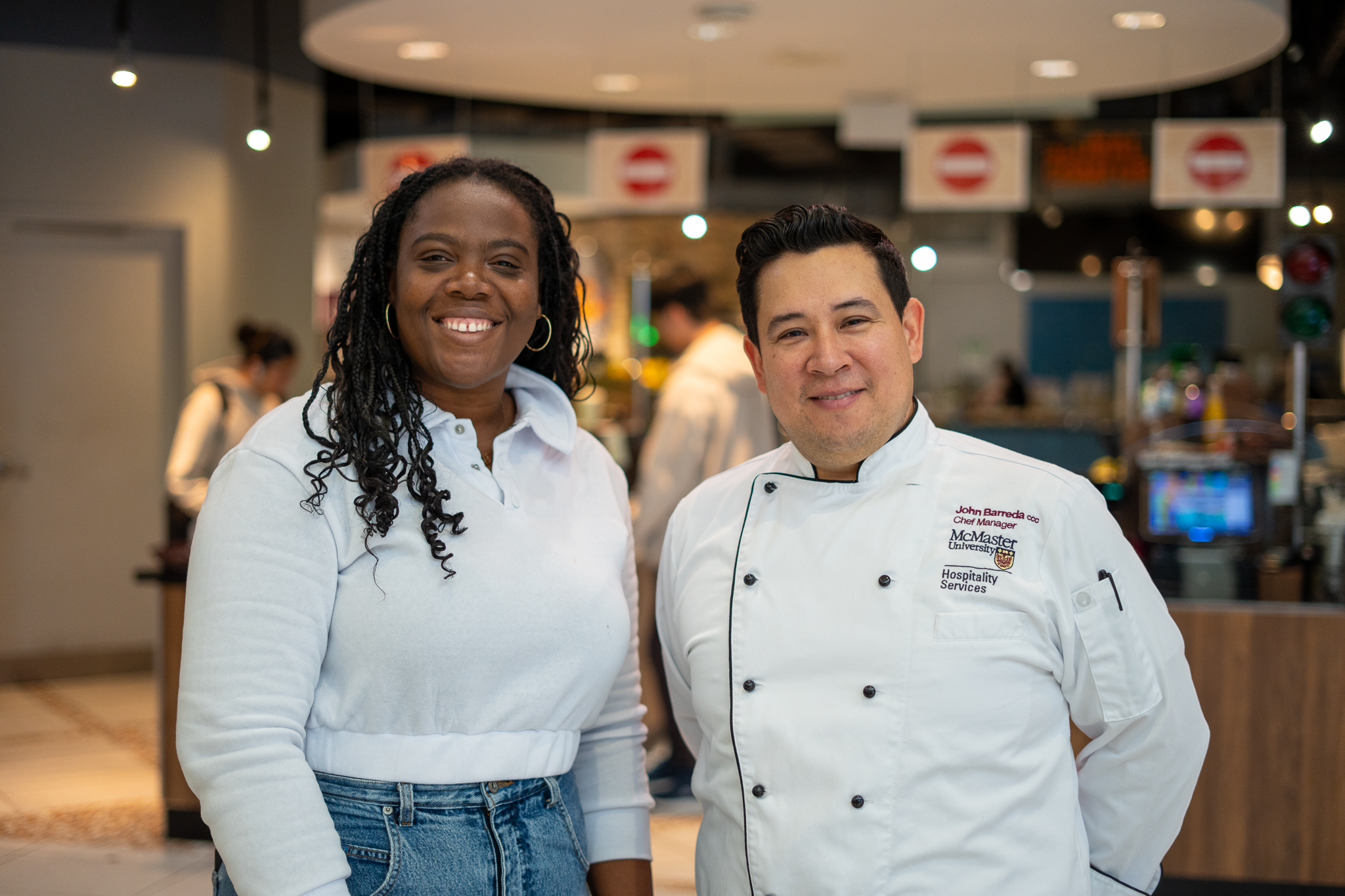 Two people, one in chef's whites stand smiling at the camera