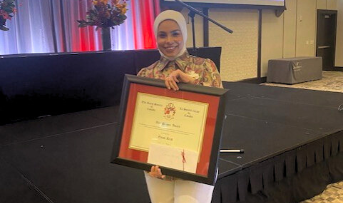 A person stands in front of a stage, holding up a big, framed award.