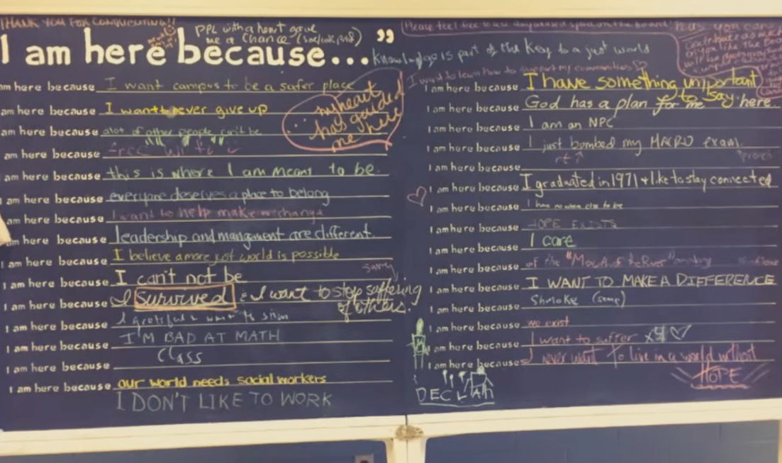 A chalkboard with dozens of "I am here because..." prompts that different people have filled out to finish the sentence.