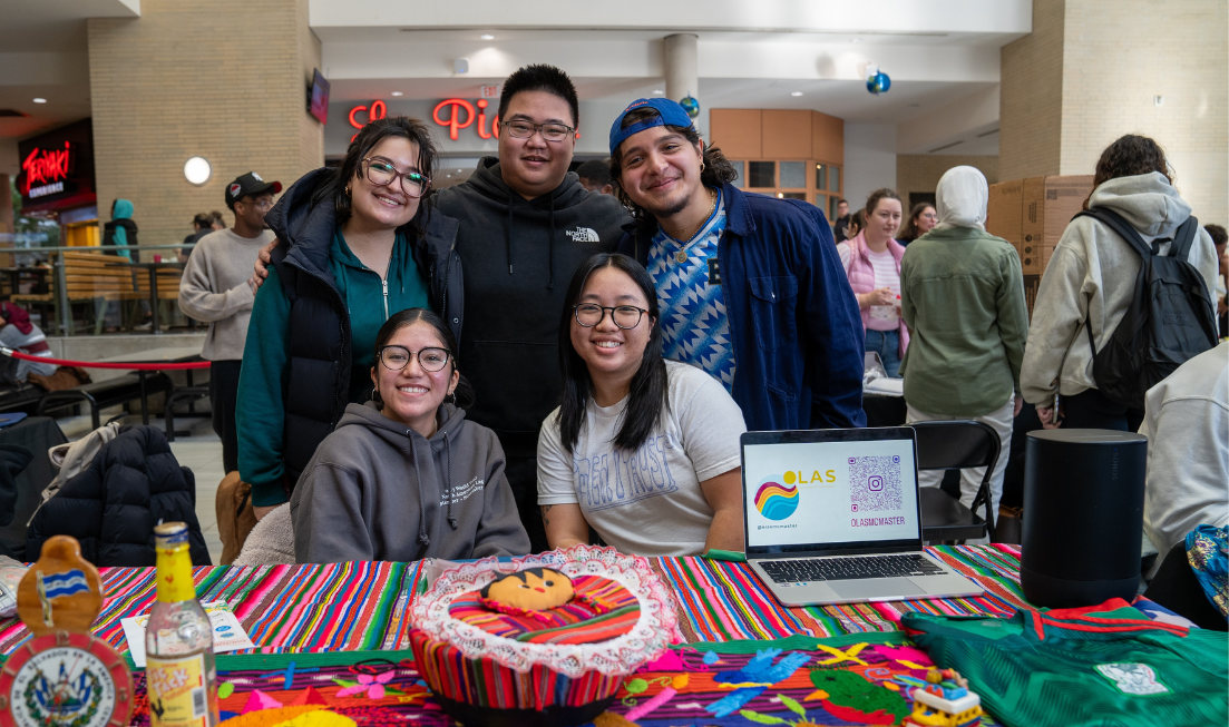 A group of five students smiles behind a gaily decorated table in MUSC