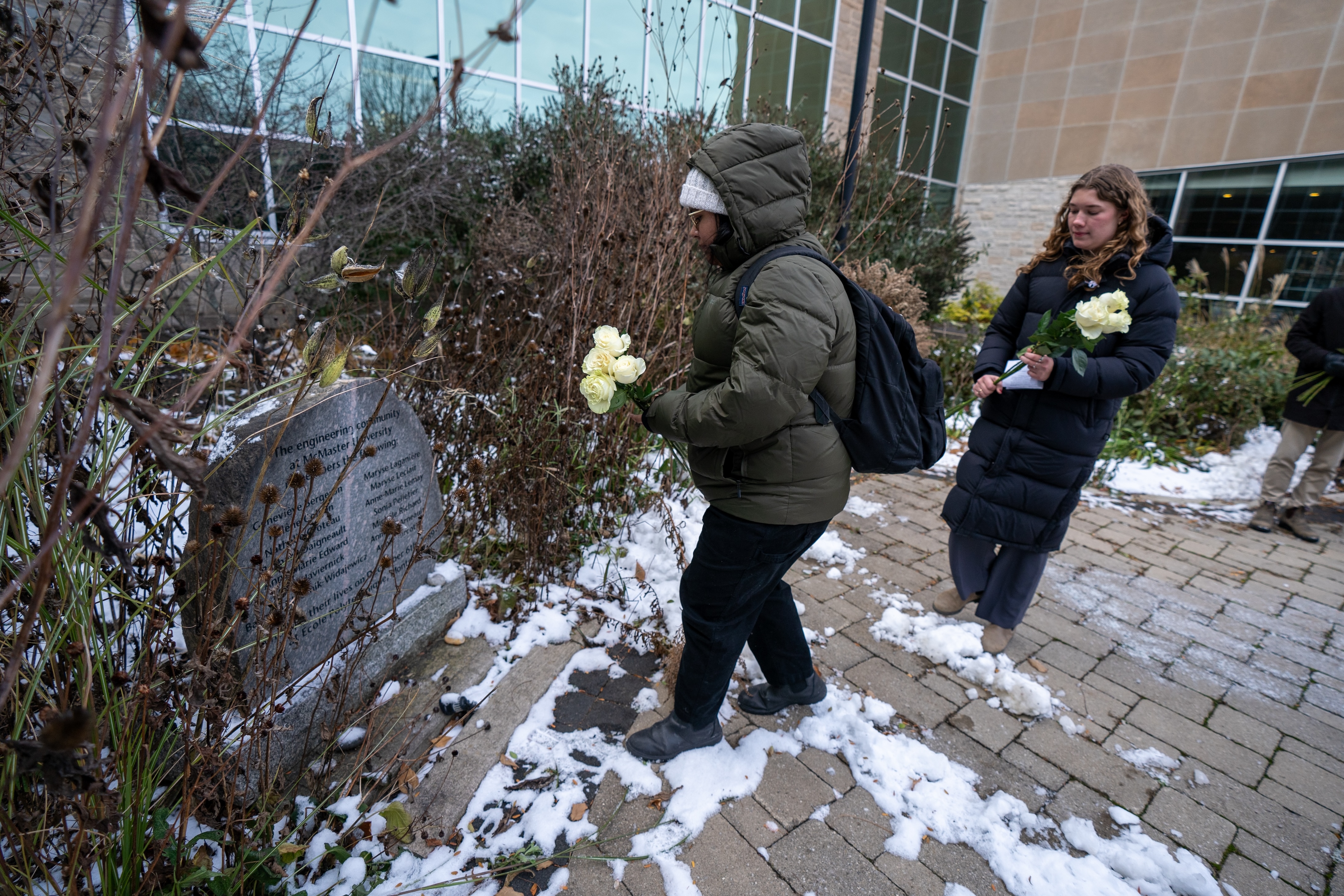 Two students holding white roses prepare to lay them at a memorial stone outside John Hodges Engineering building. 