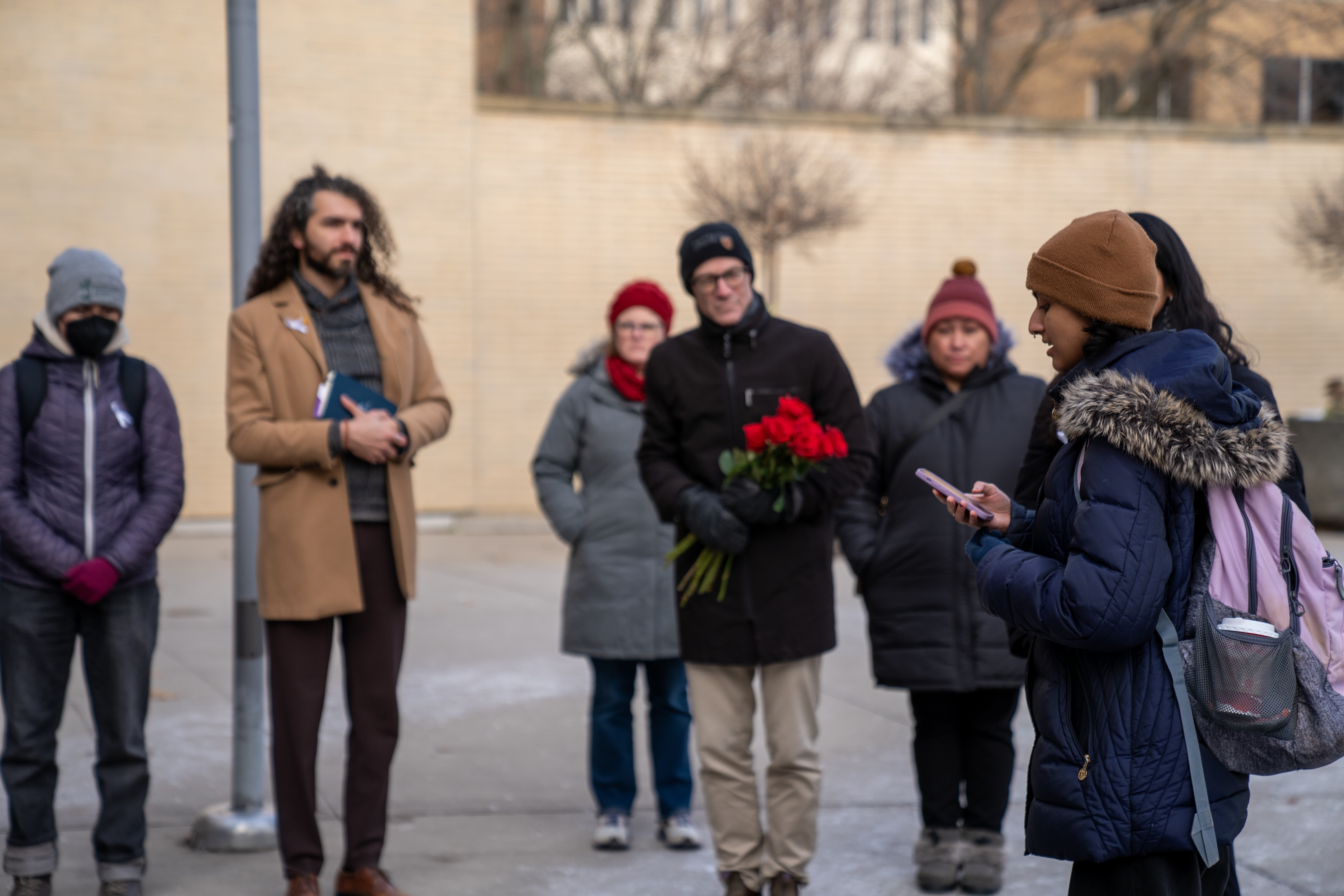 a student reads their remarks as other participants in the memorial walk listen at a stop outside the student centre.