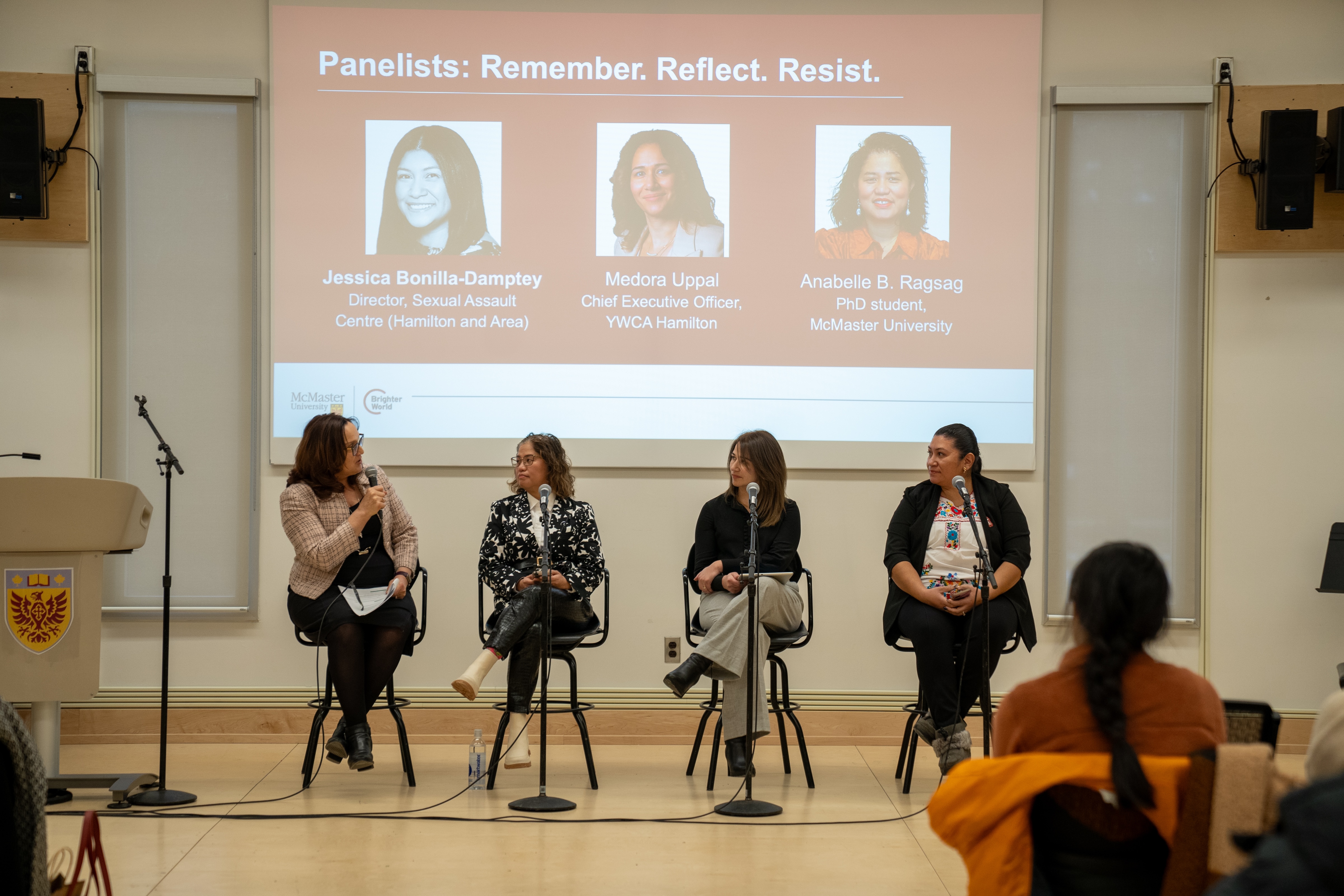 Three panelists and moderator Lenore Lukasik sit in chairs front of a screen in a classroom.