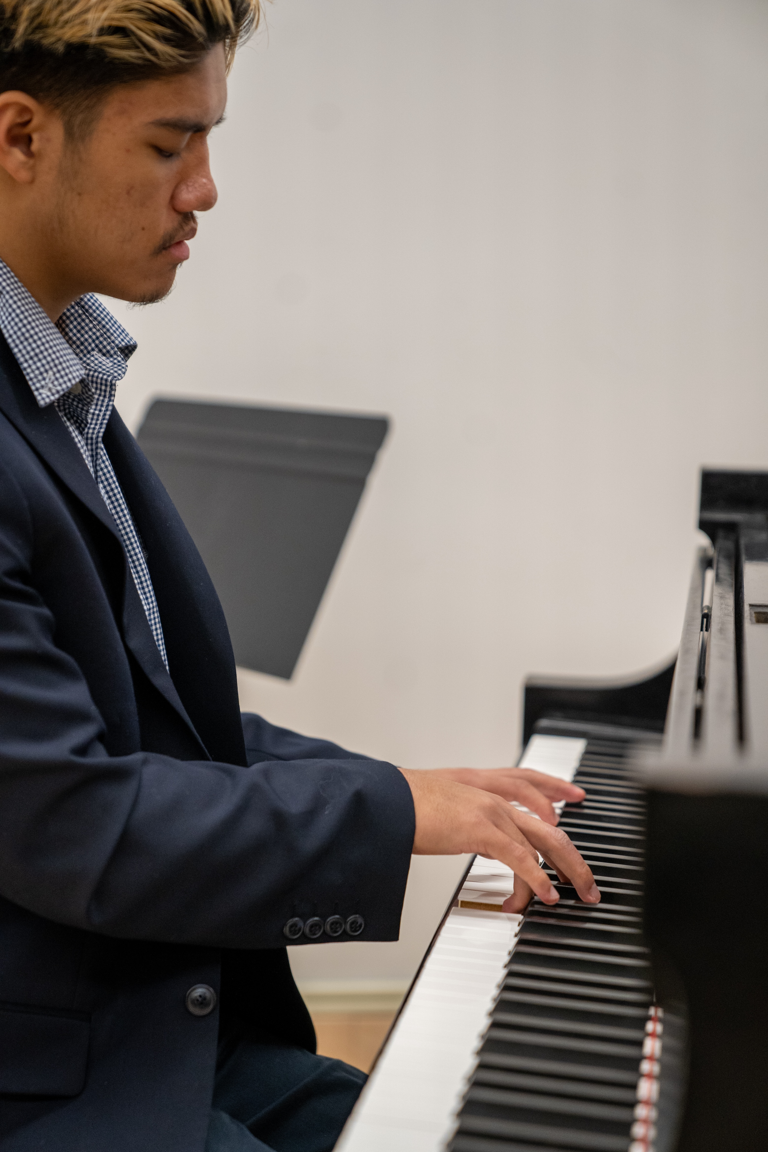 A student in a suit plays the piano indoors