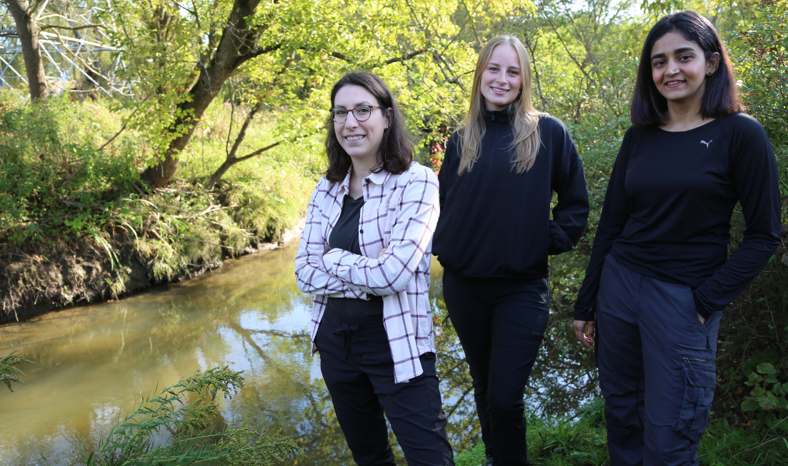 Three people standing beside a creek smiling at the camera 