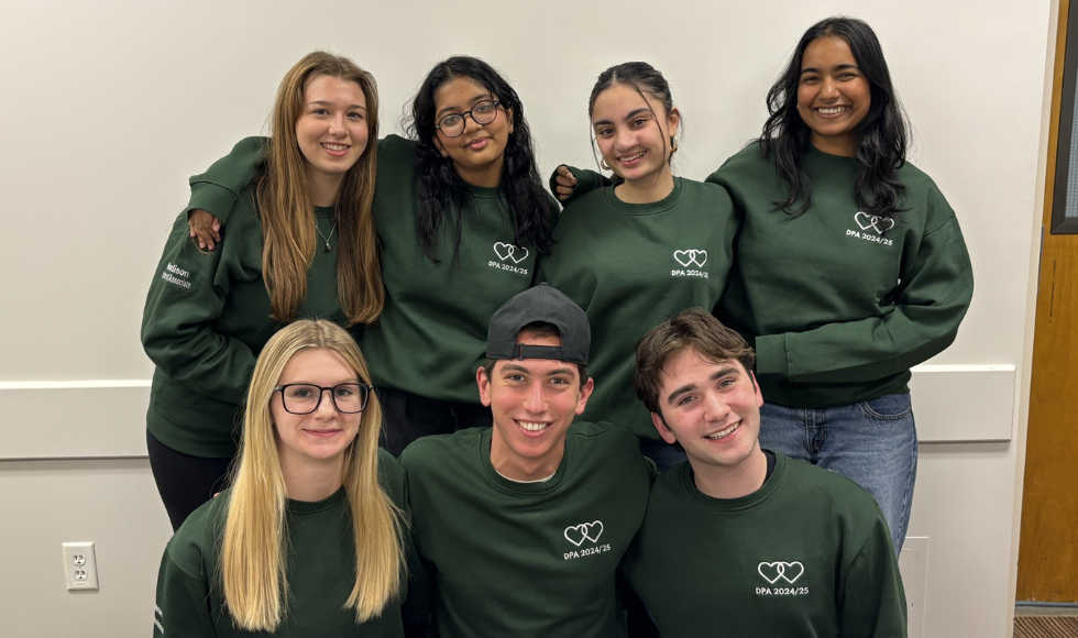 Seven people wearing matching green sweaters smile at the camera.