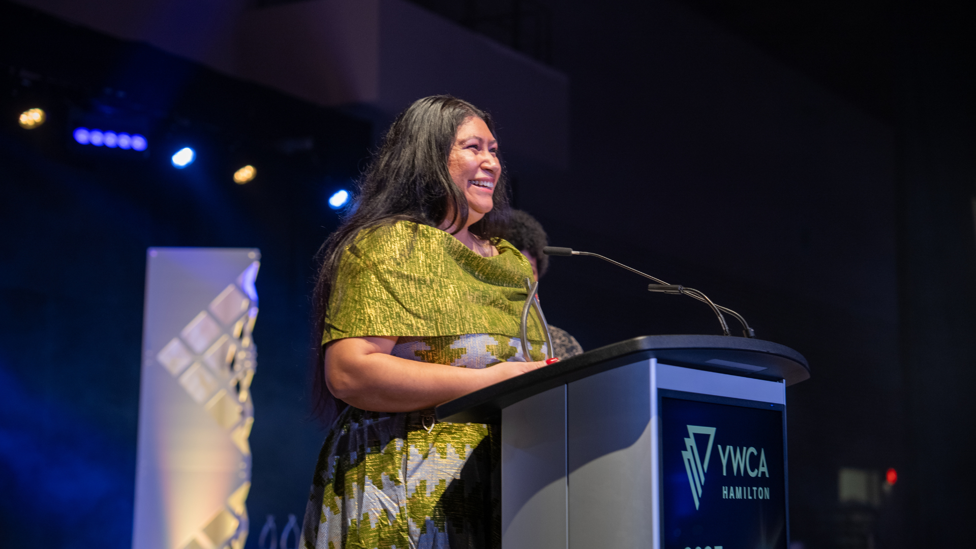 A woman stands at a podium, smiling. 