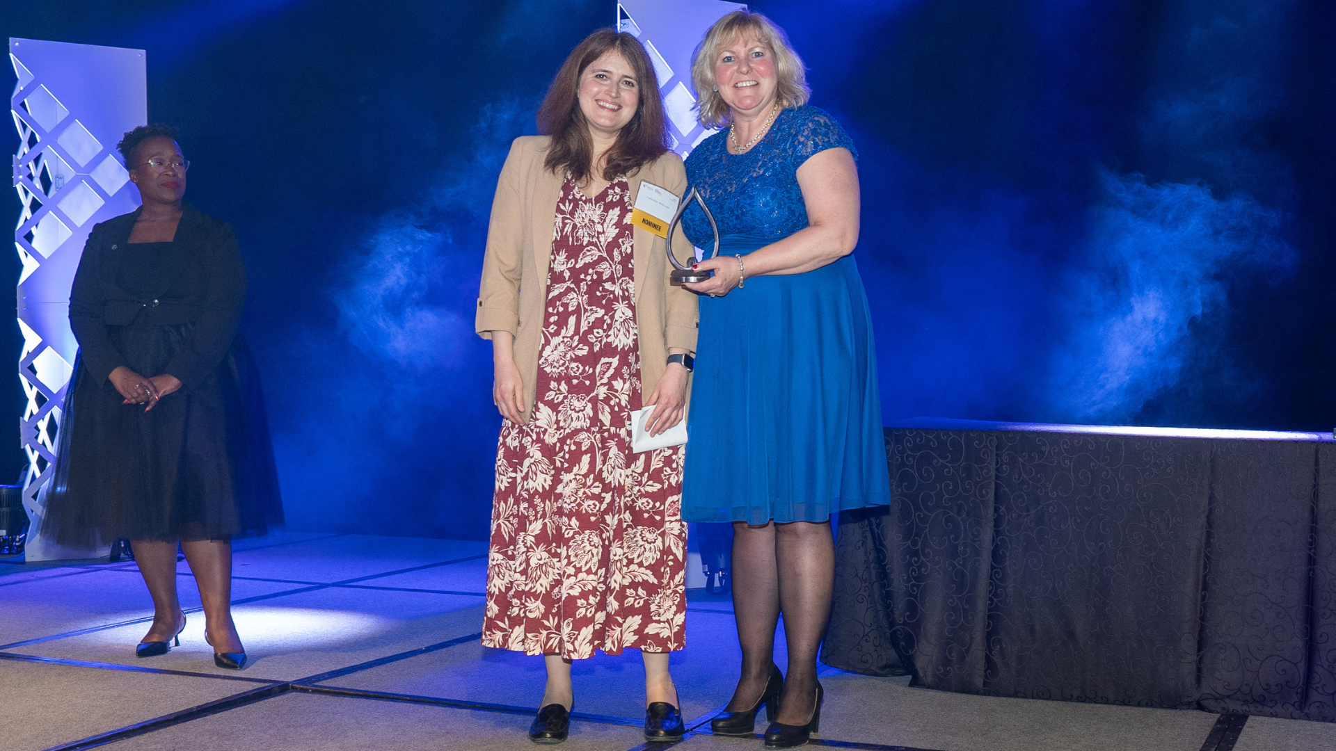 Two women stand on stage, as one presents the other with an award. 