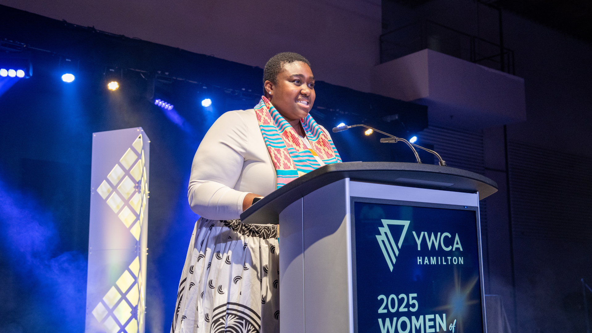 A woman stands on stage, speaking into a podium. 