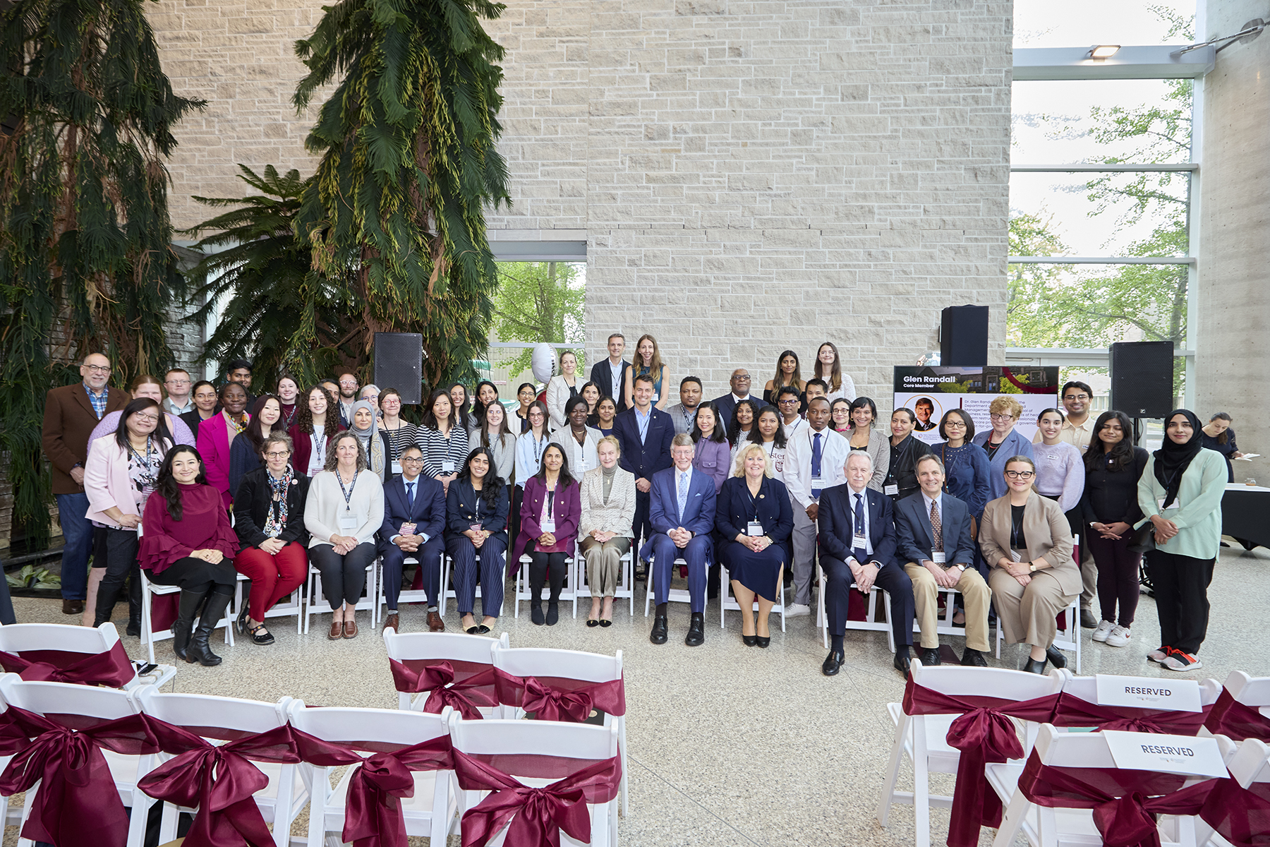 A group photo of people sitting down, posing for the camera. Chairs with ribbons are in front of them. 