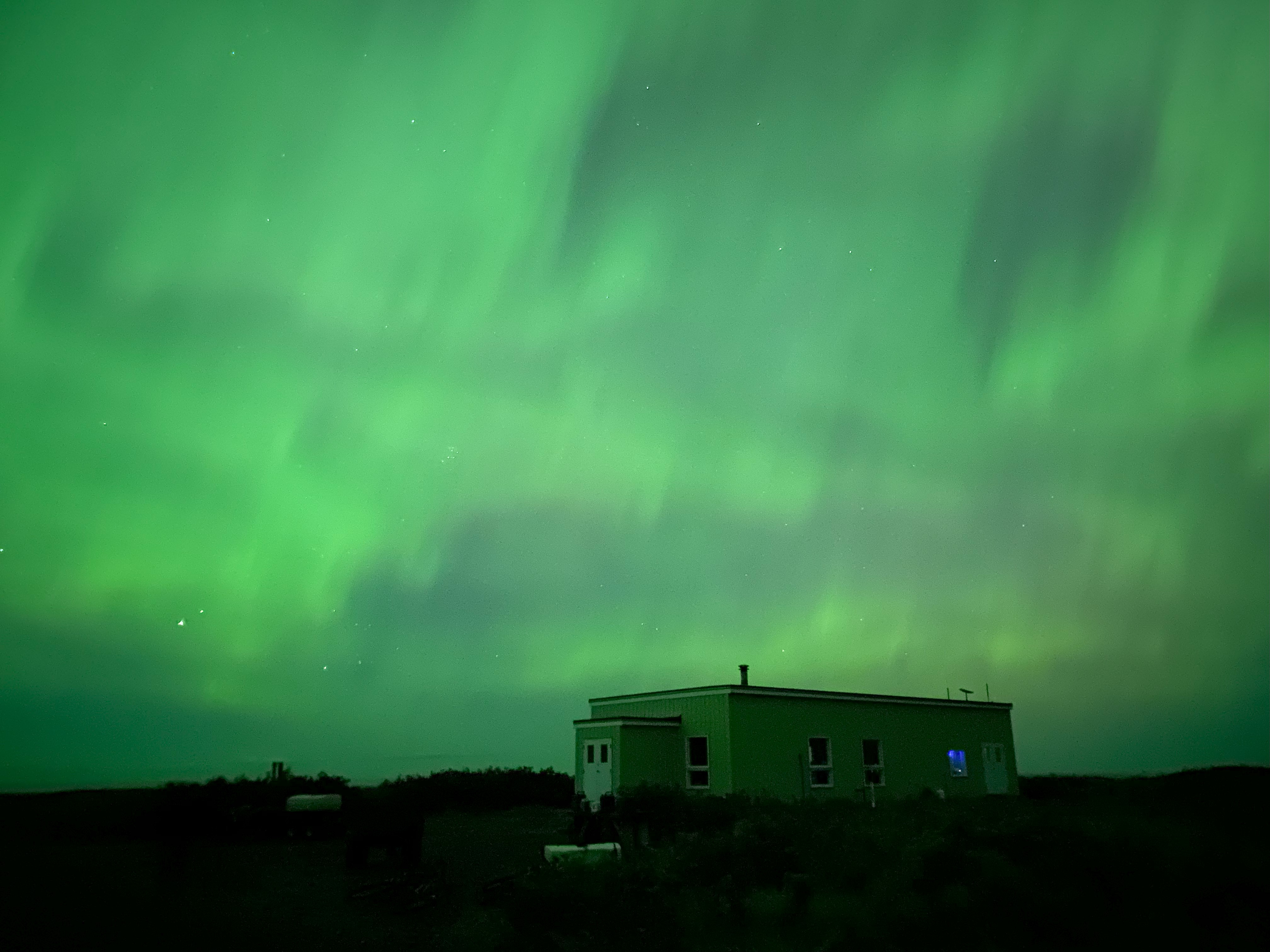 The northern lights above a small building.