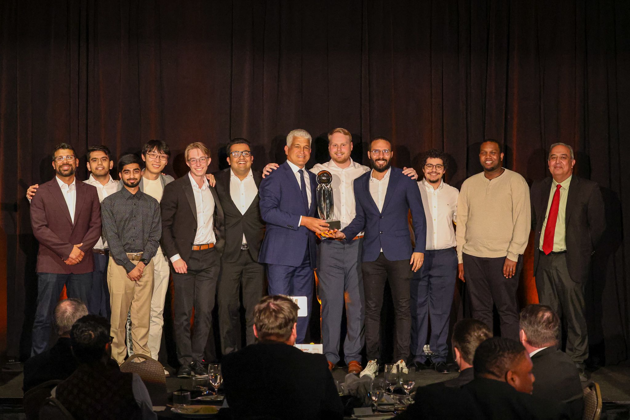 A group of men in suits stands on stage, accepting an award. 