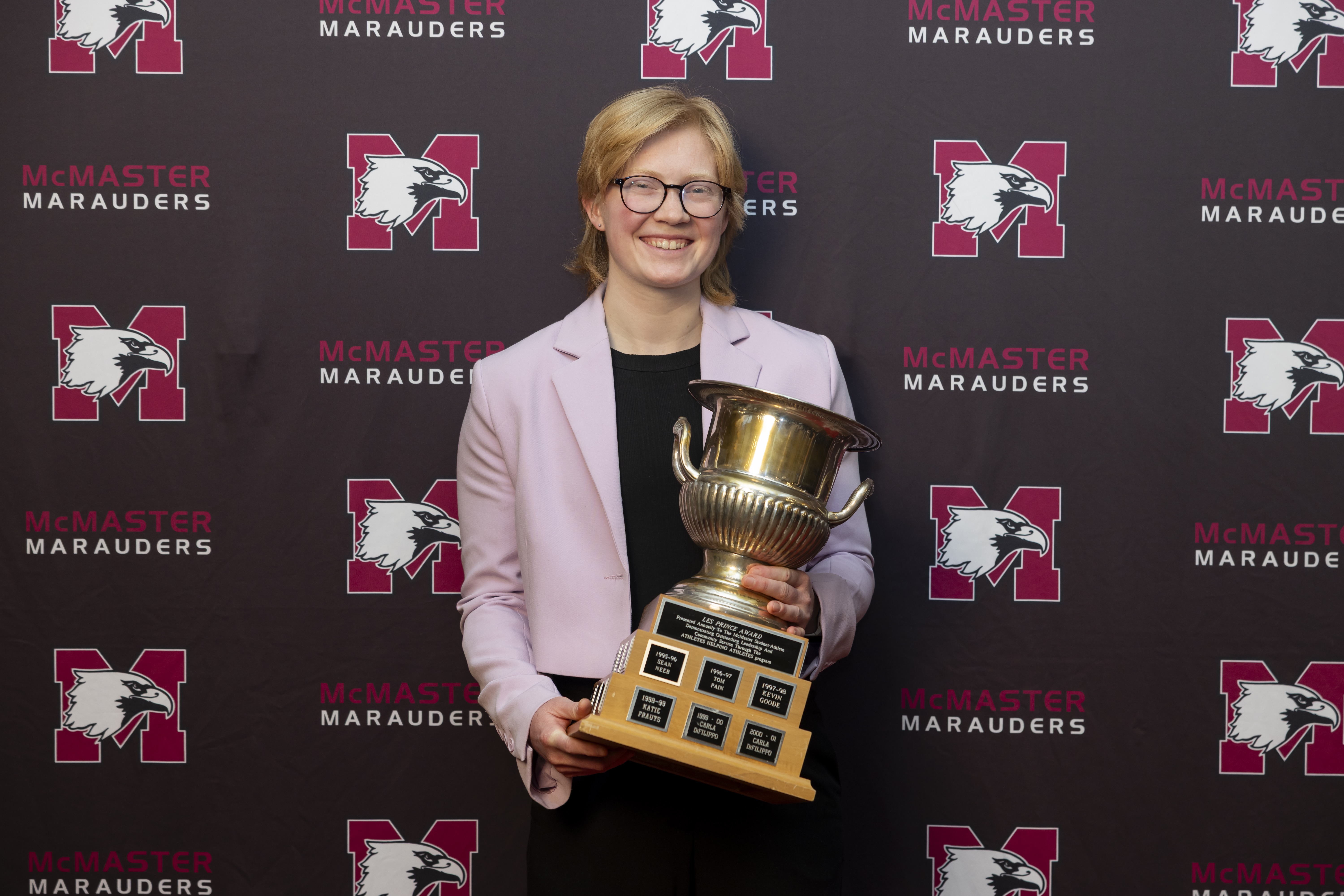 A woman in a pink blazer holds up a trophy.