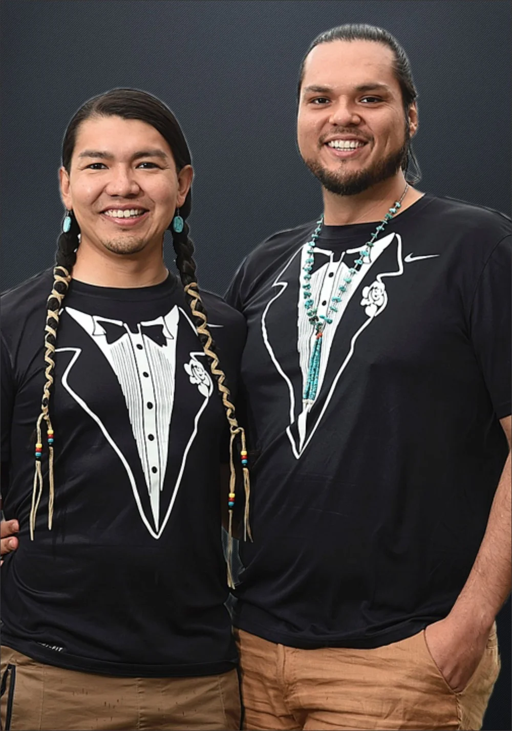 Anthony Johnson and James Makokis standing side by side in tuxedo T-shirts with their arms around each other's waists.