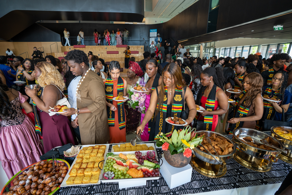 A table laden with food, with a large crowd of people behind it. 
