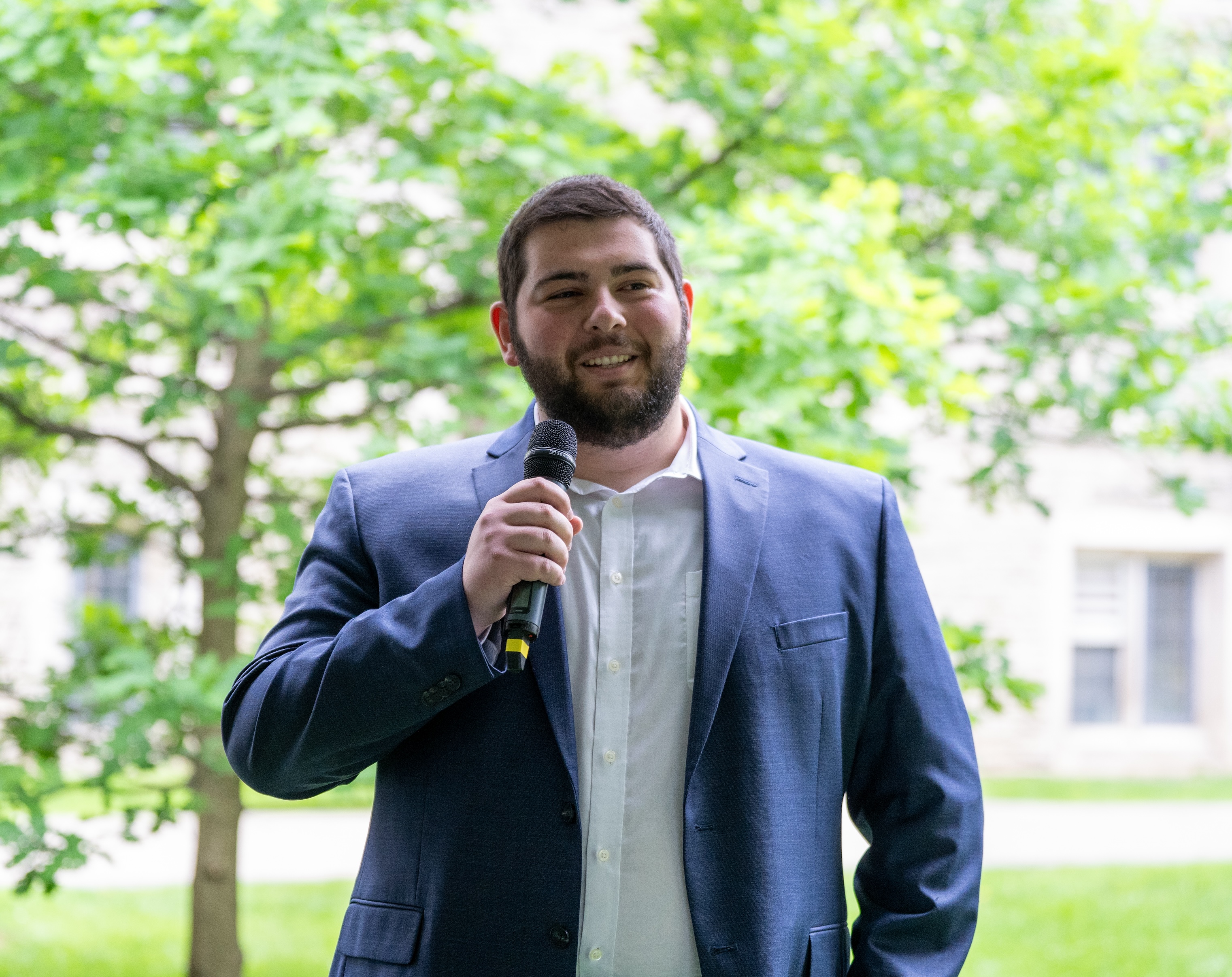 Jovan Popovic, wearing a blue suit and a white tie, smiles as he speaks into a mic.