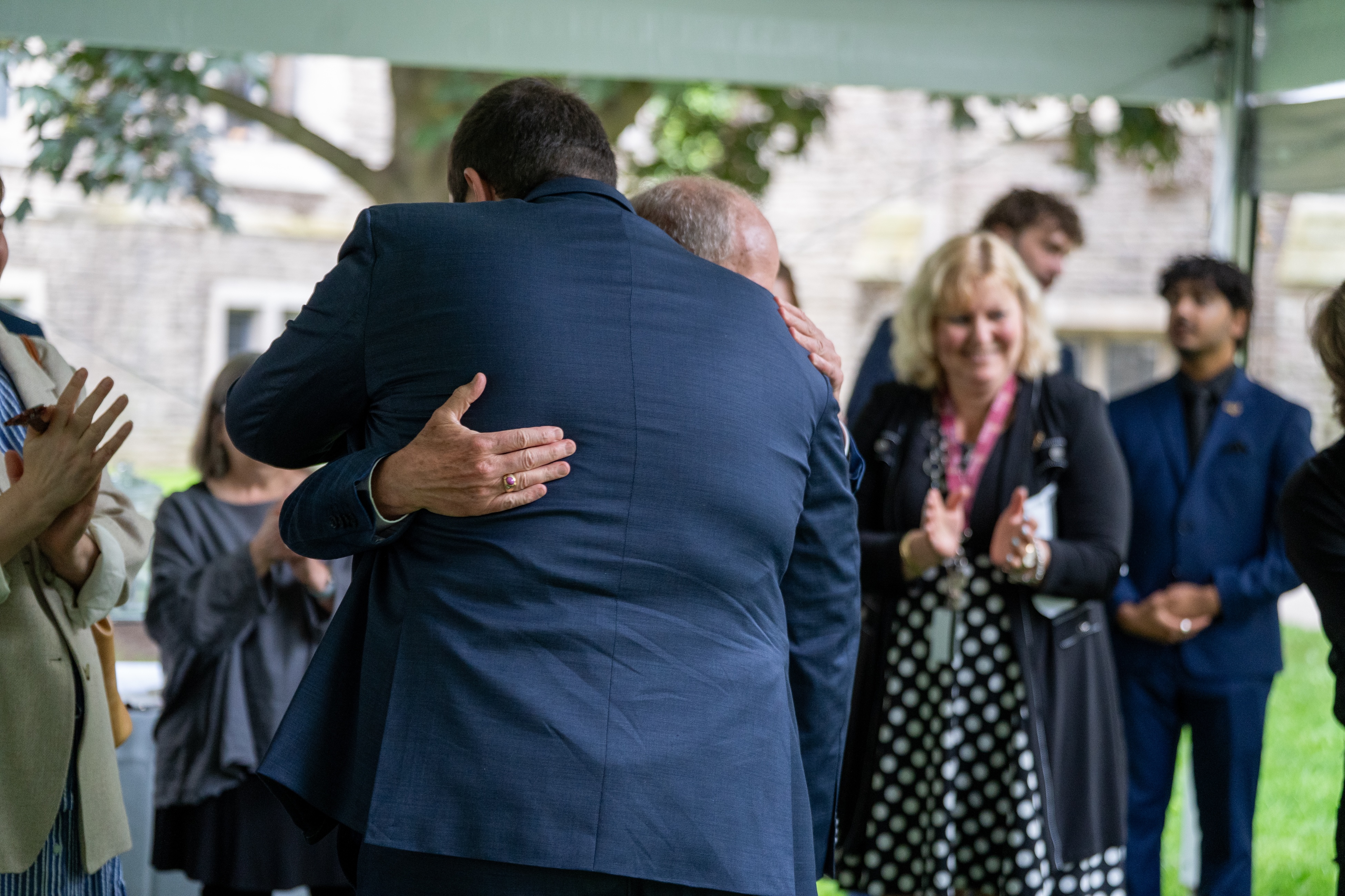 Two people hug while onlookers smile and applaud