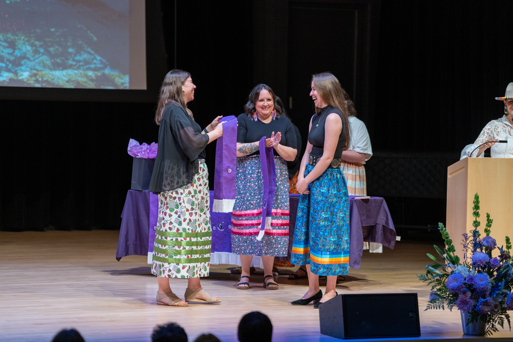 Three women stand on a stage. 