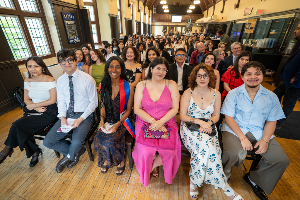 A room with many rows of seated people, in dress clothes.