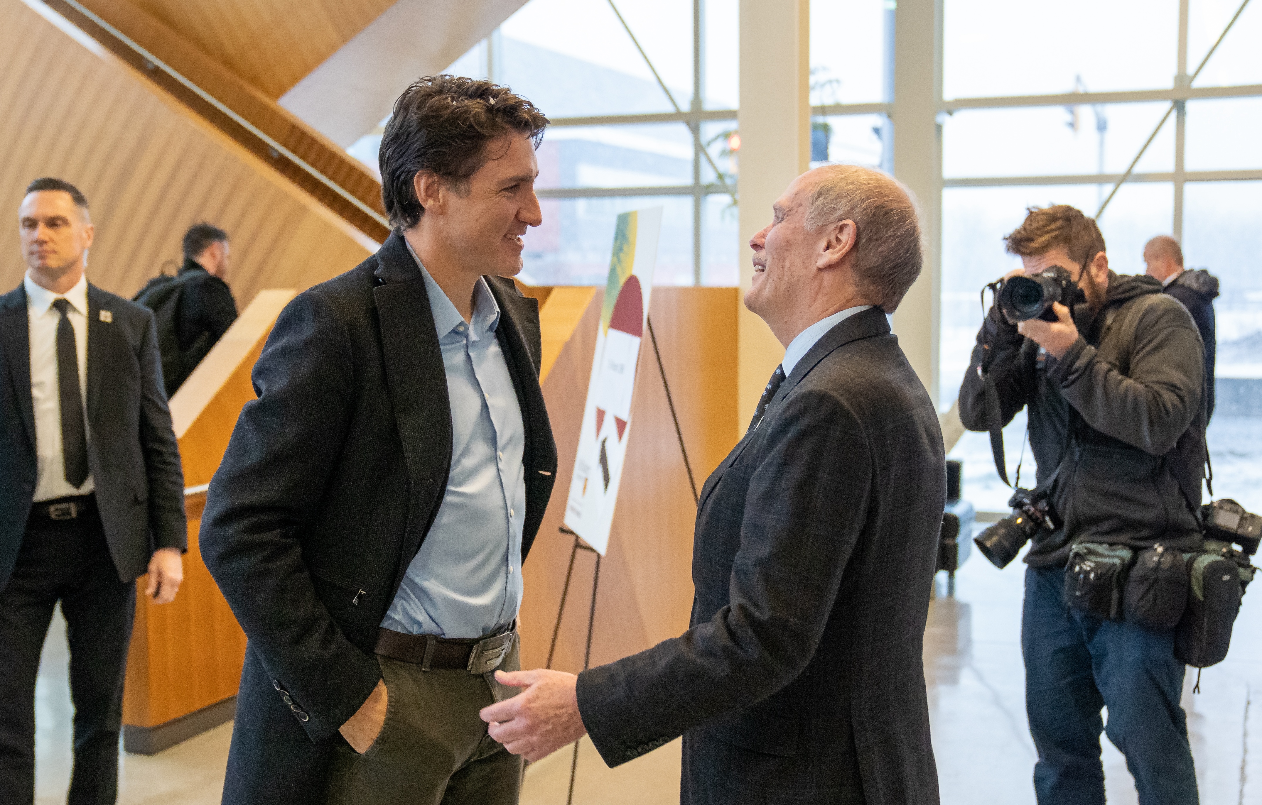 Prime Minister Justin Trudeau and McMaster President David Farrar smiling and chatting indoors, watched by others.