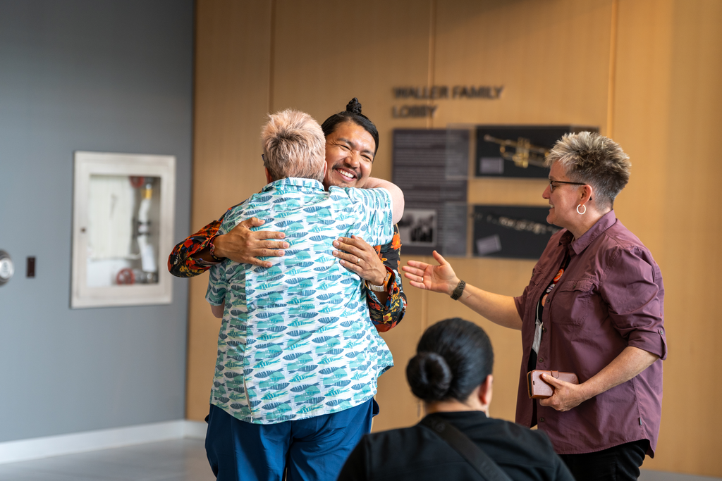Two people hug, with a third person standing beside them.