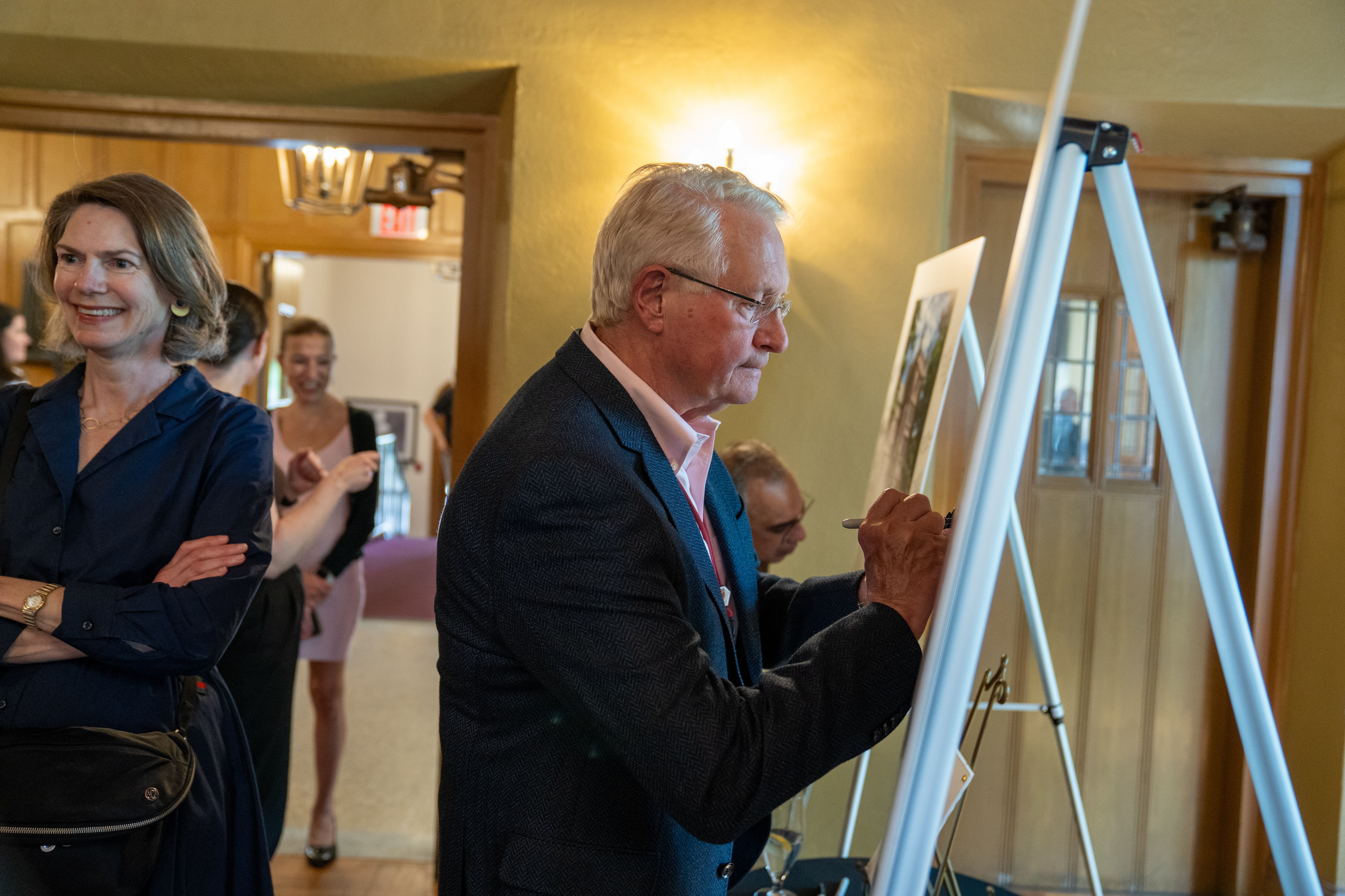 John Kelton signs a posterboard on an easel during a gathering in Alumni Memorial Hall