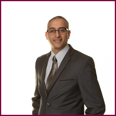 Headshot of a man in a suit wearing glasses.