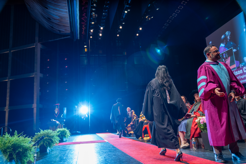 At a graduation ceremony, a woman in robes crosses the stage. 