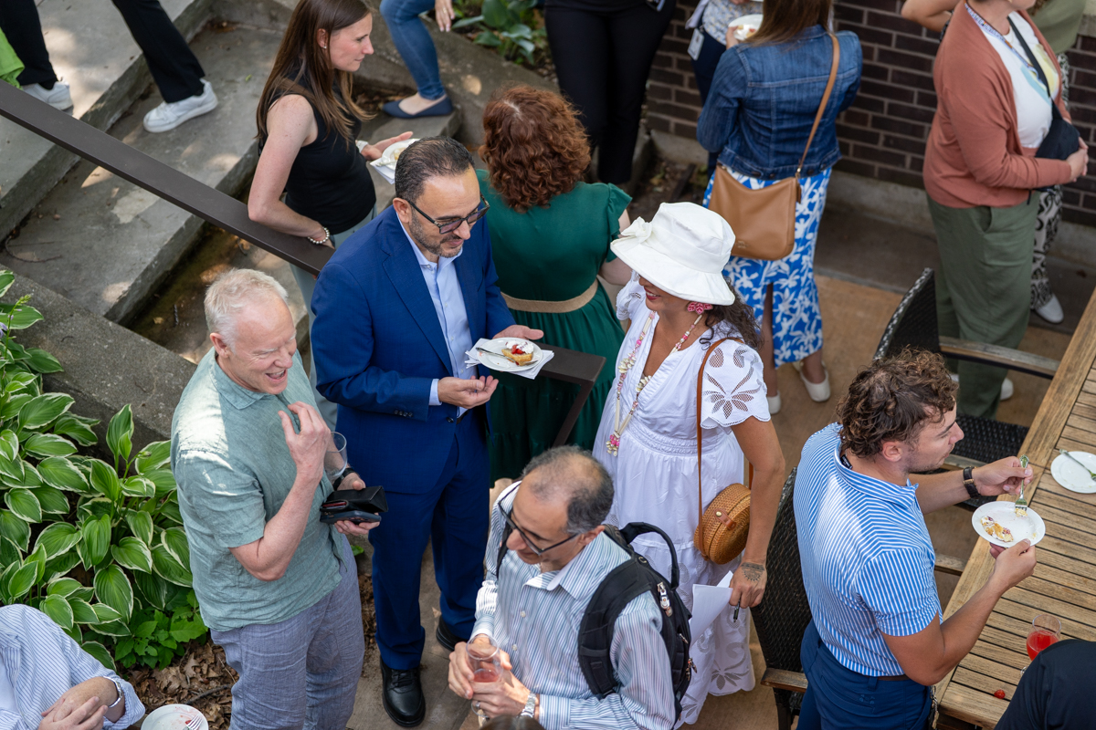Seen from above, several dozen people sit, stand and chat on the patio of the Buttery.