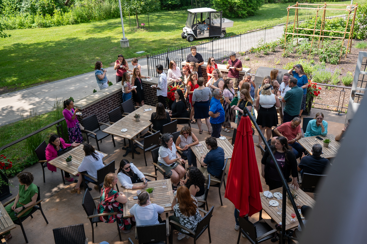 Seen from above, several dozen people sit, stand and chat on the patio of the Buttery.