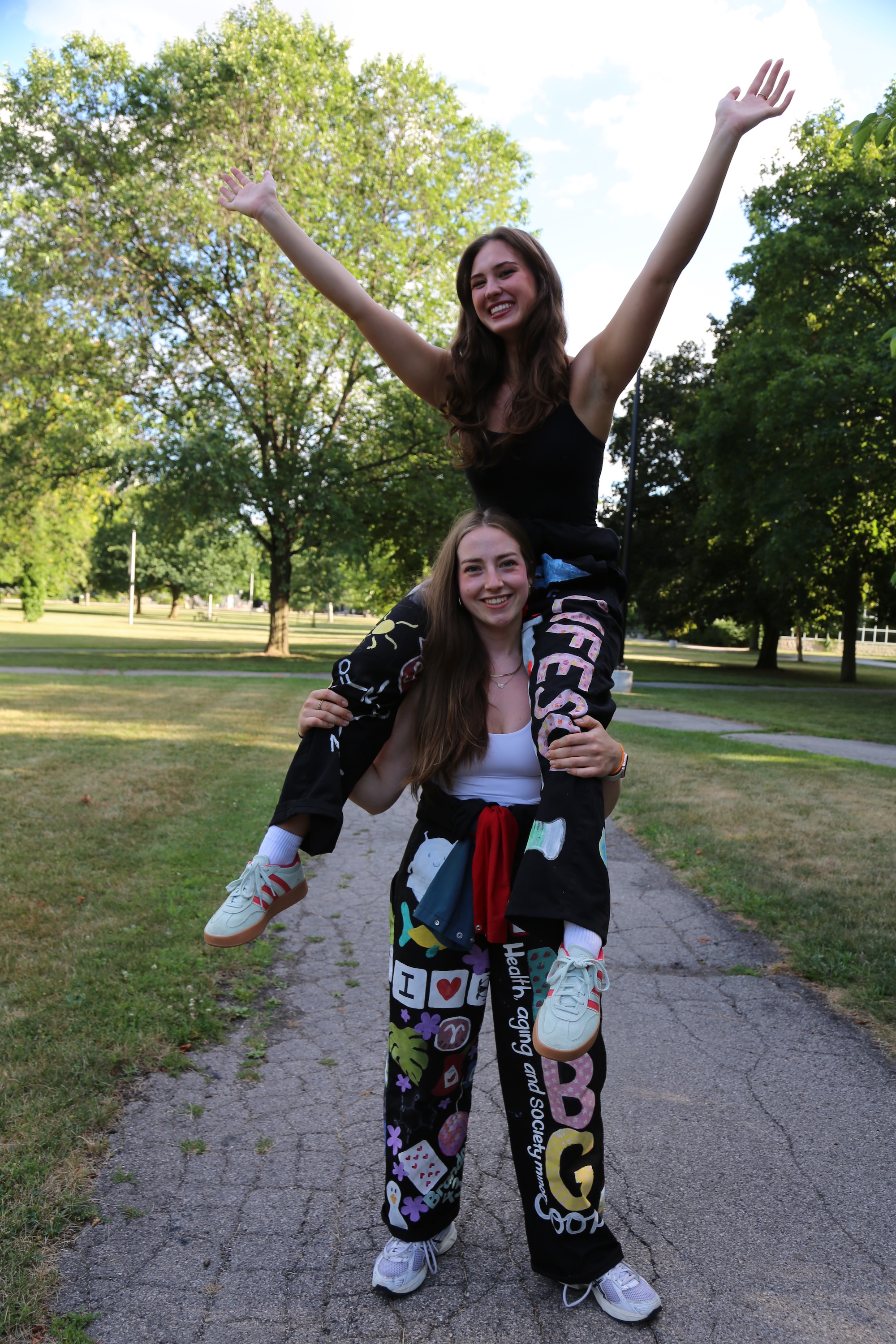 A woman sits on another woman's shoulders, on a path outdoors. 